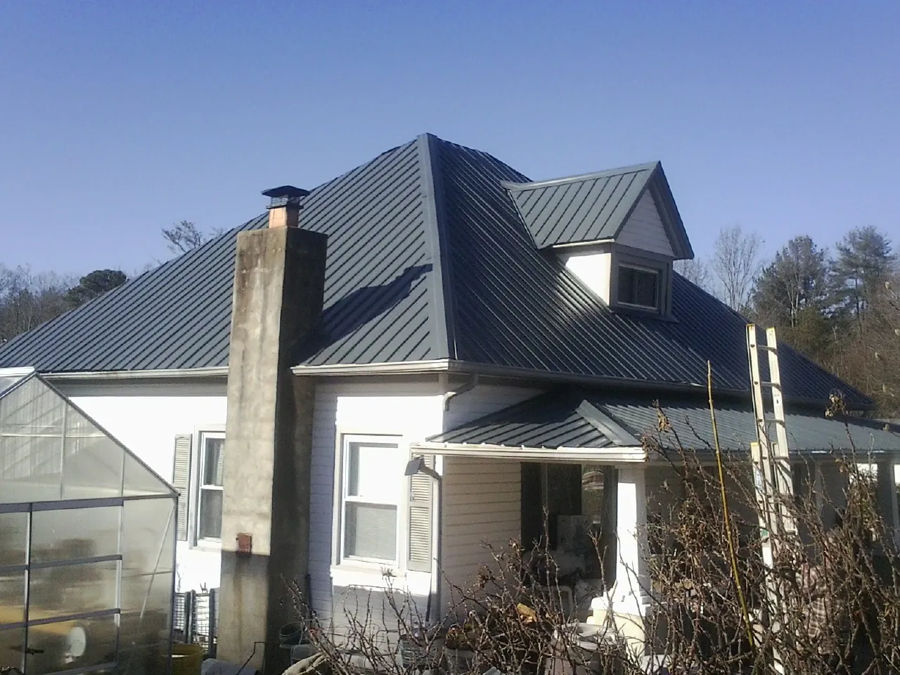 Dark blue standing seam metal roof on a white farmhouse with dormer — Slate & Tile Roof Repair by Roofing Brothers in Battery Park