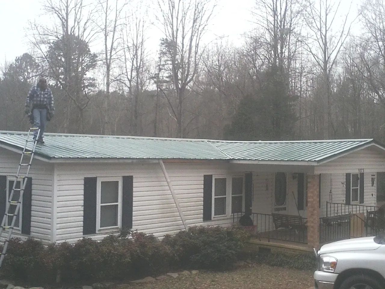 Worker on a ladder beside a new green metal roof on a ranch home in Battery Park