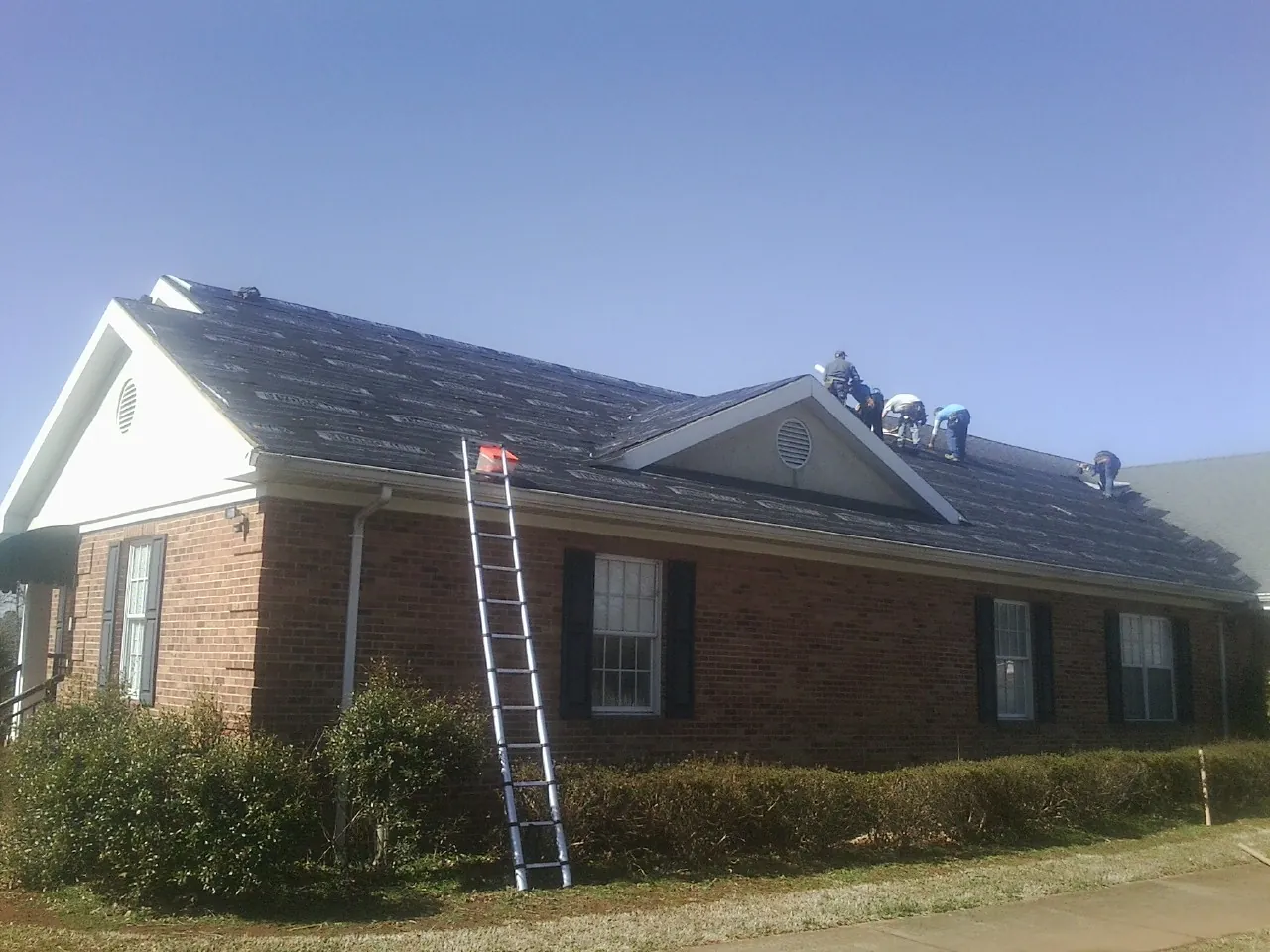 Crew tearing shingles off a brick ranch roof with a ladder set — Emergency Roof Repair work by our crew in Battery Park