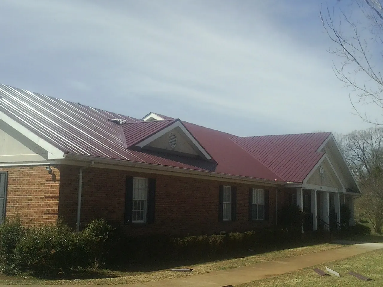 Red metal roof with gabled entries on a long brick building, from a Hail Damage Roof Repair job in Battery Park
