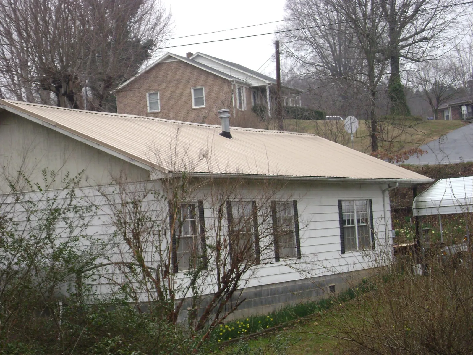 Tan metal roof on a white sided house set into a hillside — Commercial Roofing by Roofing Brothers in Battery Park