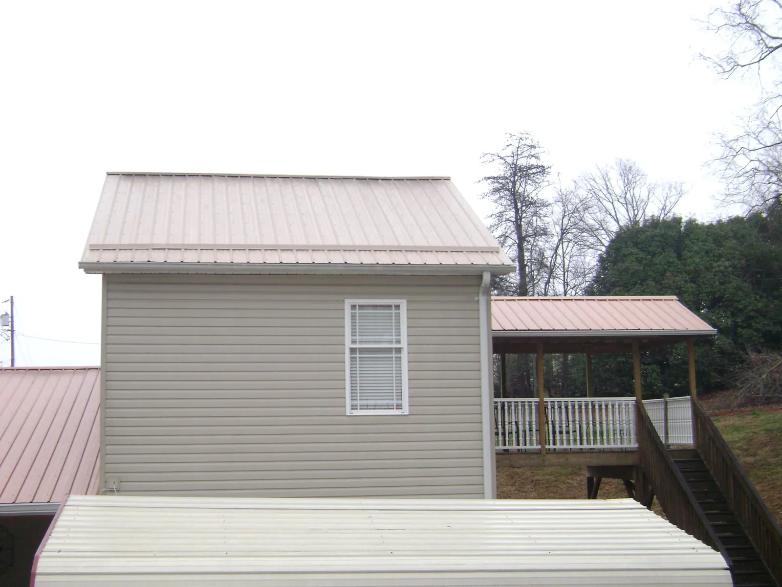Tan metal roofs on a two story addition and attached porch, from a Roof Replacement job in Battery Park